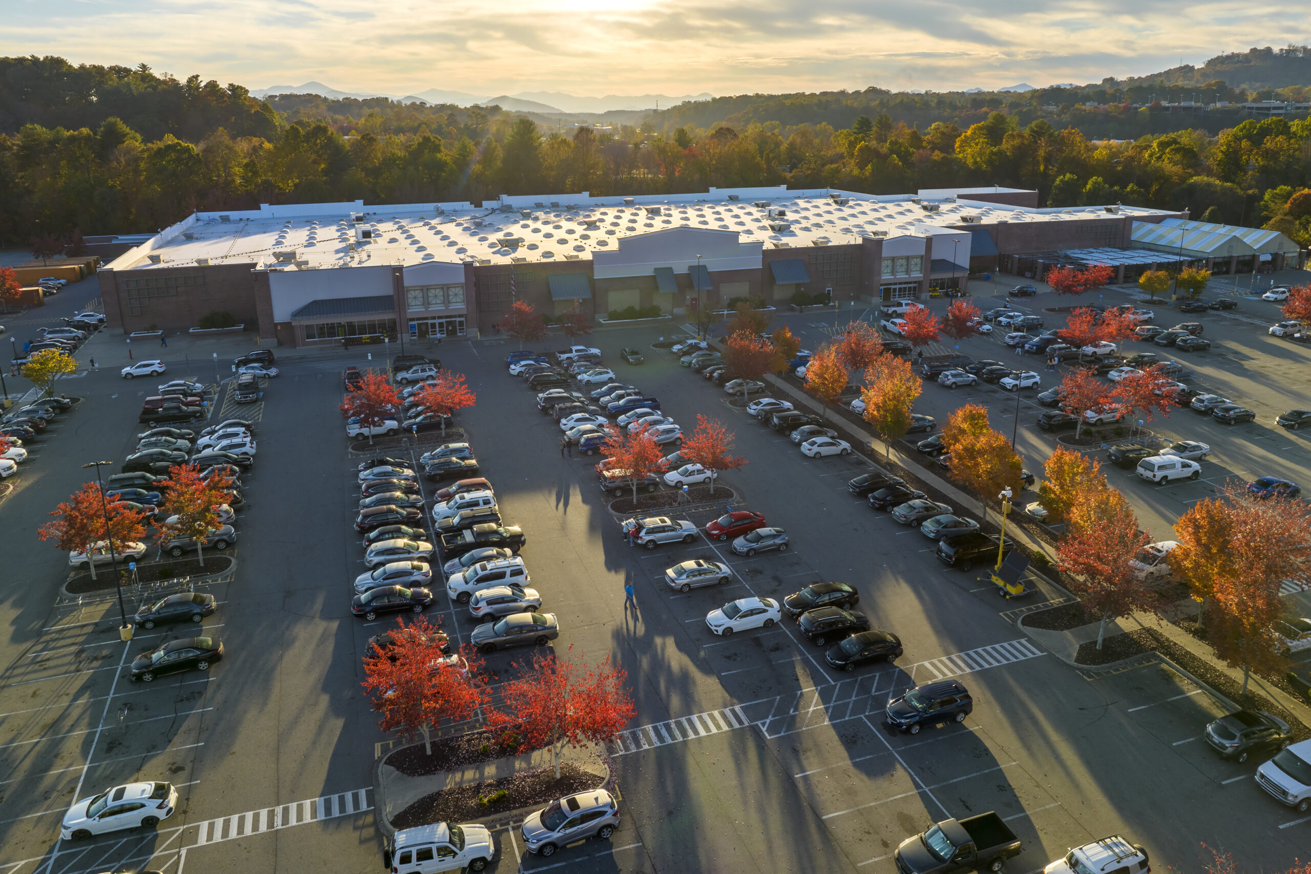 Top view of many cars parked on a parking lot in front of a strip mall plaza. Concept of consumerism and market economy.